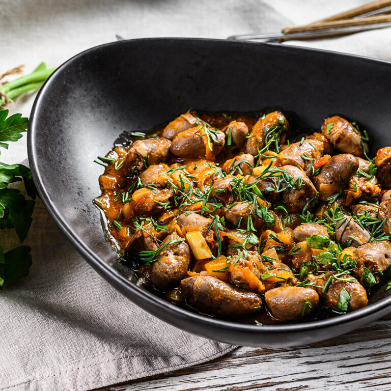 Stewed chicken liver hearts in a plate.  White wooden background