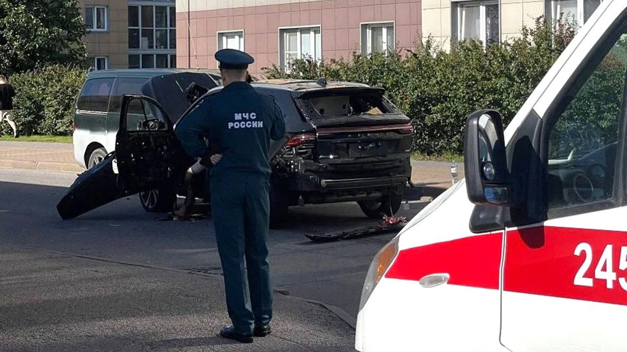 Співробітник МНС Росії стоїть біля пошкодженого чорного автомобіля та швидкої