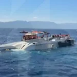 Кренящийся білий катамаран з пасажирами в жилетах і рятувальними човнами в морі