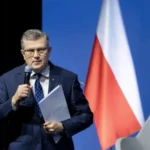 Марчин Босацький з мікрофоном і документами на фоні прапорів Польщі та ЄС