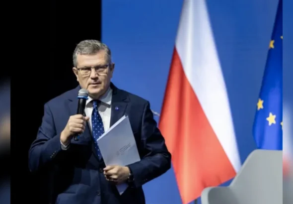 Марчин Босацький з мікрофоном і документами на фоні прапорів Польщі та ЄС