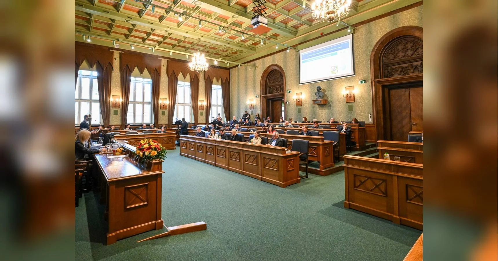 Засідання міської ради Вроцлава в історичній залі з дерев’яними лавами та екраном