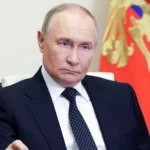 Володимир Путін у темному костюмі сидить на тлі президентського штандарта Росії