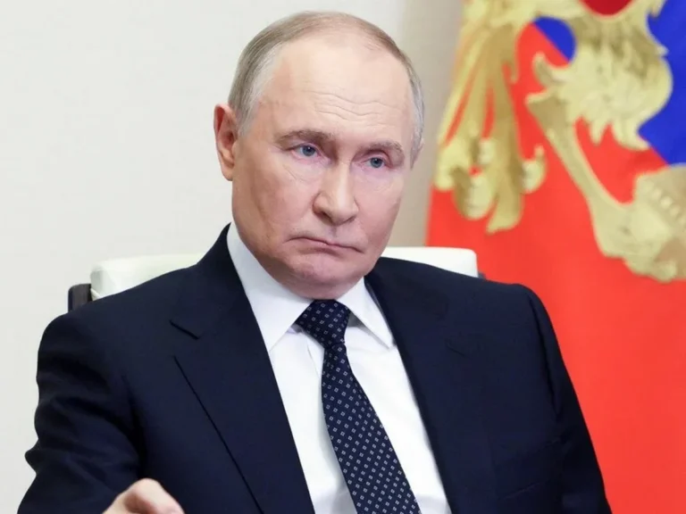 Володимир Путін у темному костюмі сидить на тлі президентського штандарта Росії