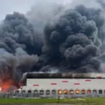 Пожежа на довгій білій промисловій будівлі з густою чорною хмарою диму