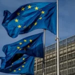 Прапори ЄС розвиваються на флагштоках біля сучасної будівлі під блакитним небом