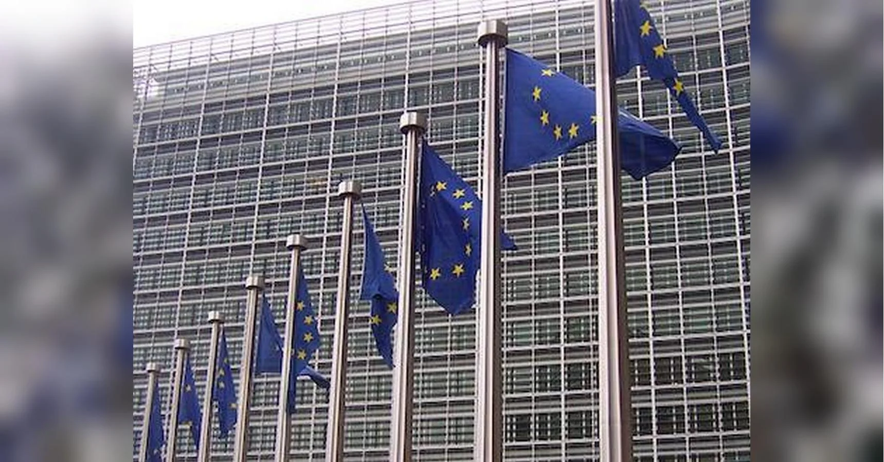 Прапори ЄС на флагштоках перед скляним фасадом європейської інституції