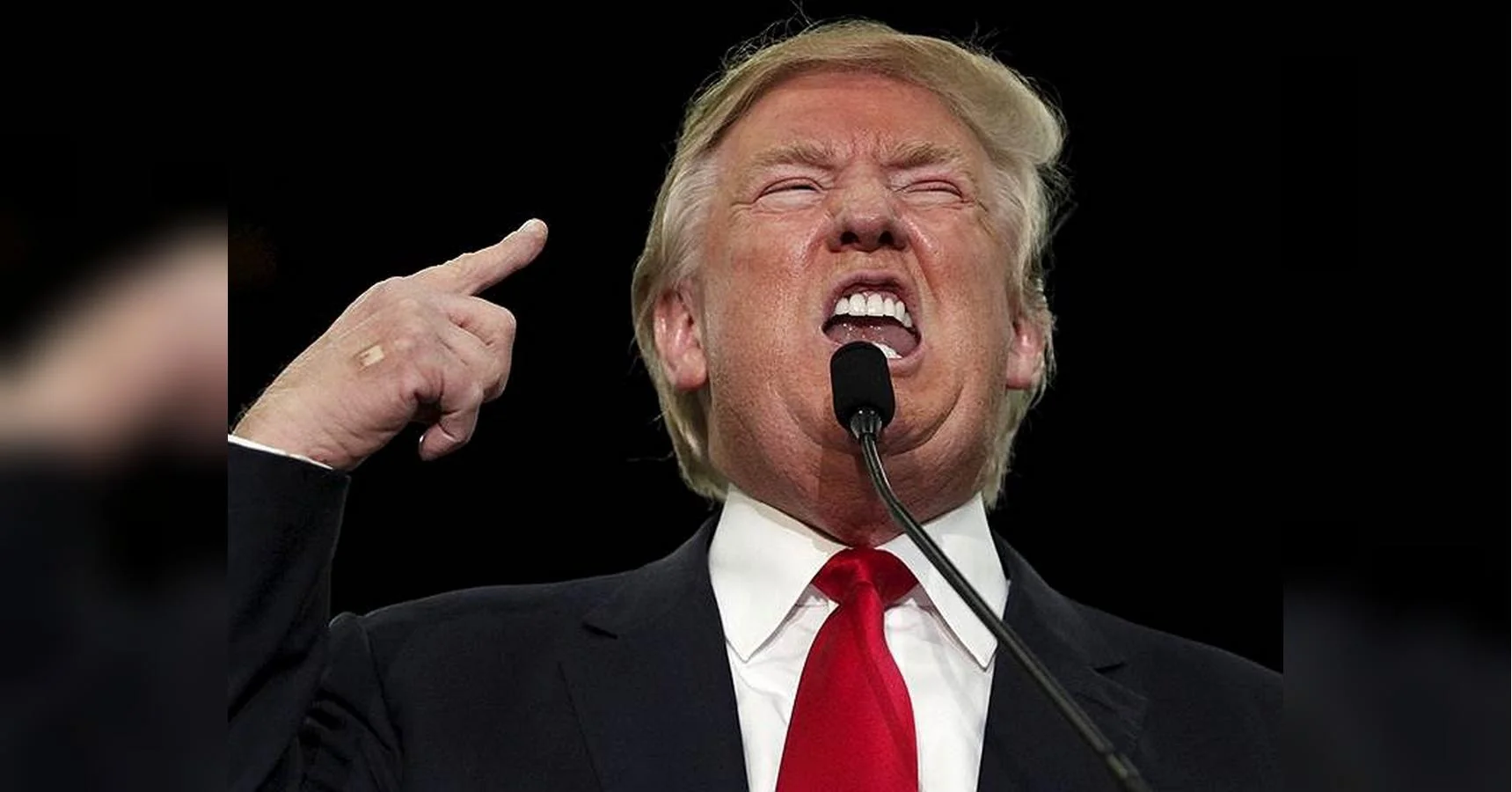 Дональд Трамп виступає з мікрофоном і вказує пальцем вгору