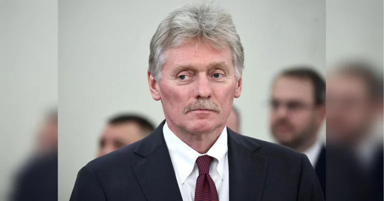 Дмитро Пєсков у темному костюмі з червоною краваткою на брифінгу