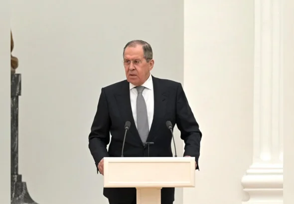 Сергій Лавров у костюмі виступає за білою трибуною з мікрофонами