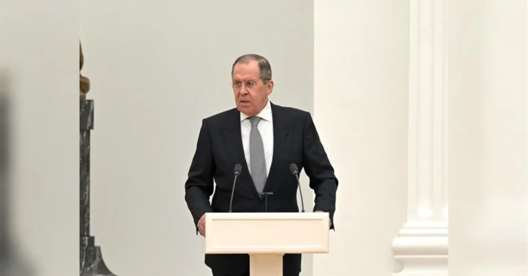 Сергій Лавров у костюмі виступає за білою трибуною з мікрофонами