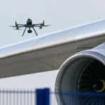 Дрон летить над крилом і турбіною літака біля синьої огорожі