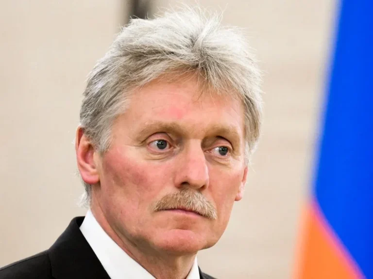 Дмитро Пєсков у костюмі на тлі російського прапора