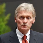 Портрет сивоволосого чоловіка з вусами в темному костюмі та червоній краватці