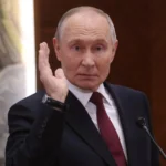 Володимир Путін у темному костюмі підняв руку біля мікрофонів