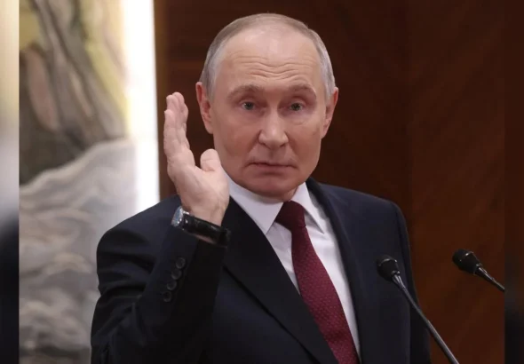 Володимир Путін у темному костюмі підняв руку біля мікрофонів