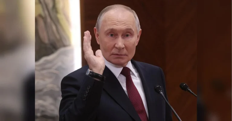Володимир Путін у темному костюмі підняв руку біля мікрофонів