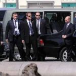 Путін стоїть біля чорного авто в оточенні охоронців і військового