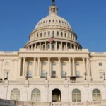 Капітолій США з білим куполом і прапором на тлі блакитного неба