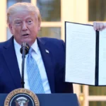 Трамп біля президентської трибуни тримає розгорнутий підписаний документ