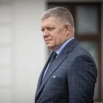 Роберт Фіцо в клітчастому костюмі стоїть біля світлої стіни з вікном