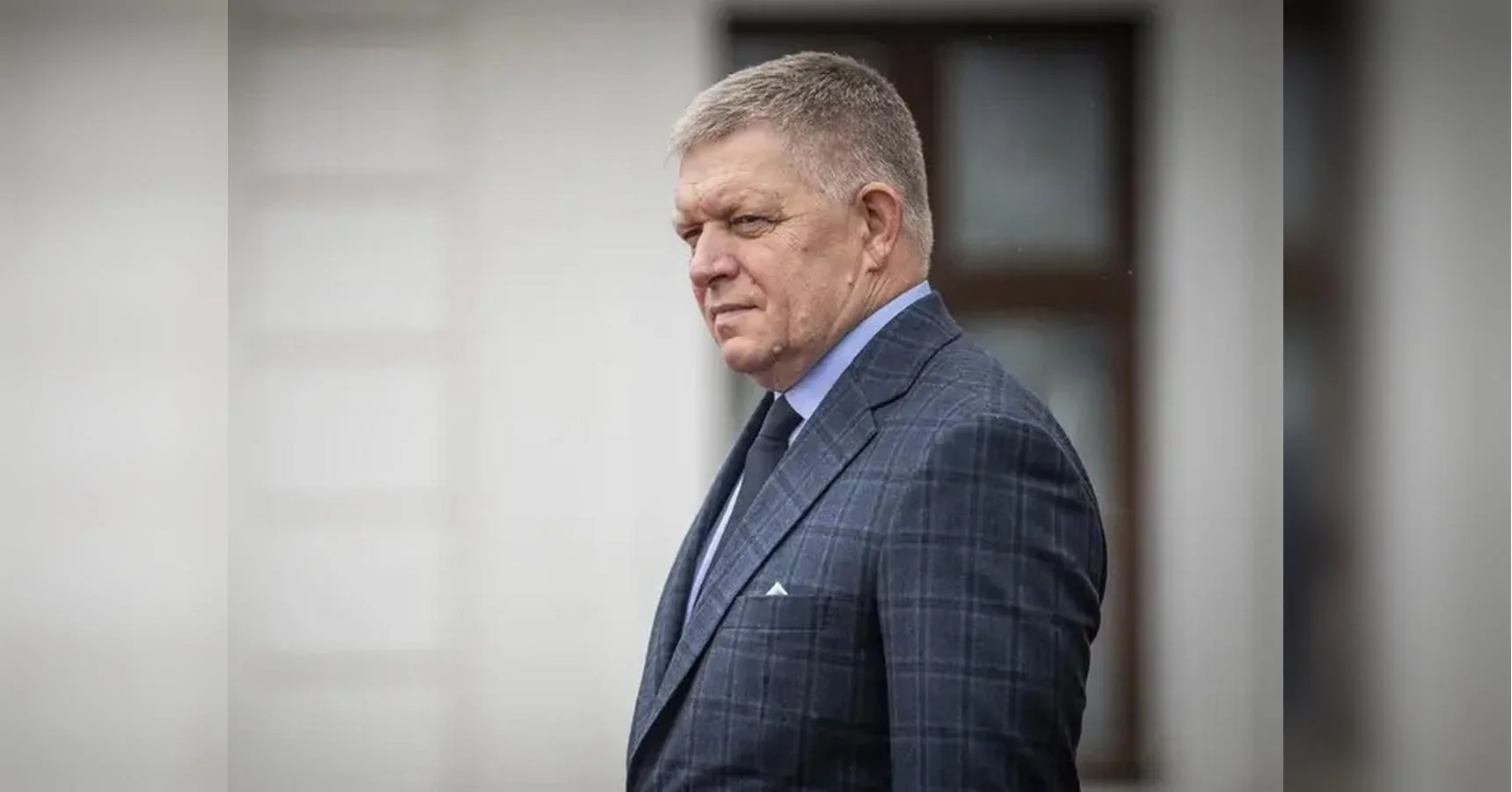 Роберт Фіцо в клітчастому костюмі стоїть біля світлої стіни з вікном