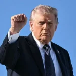 Дональд Трамп у темному костюмі підняв кулак на тлі блакитного неба