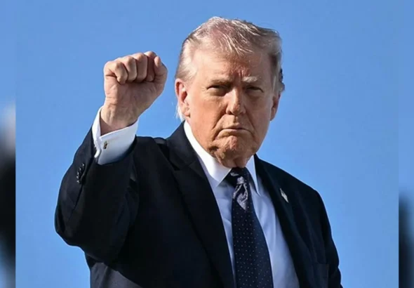 Дональд Трамп у темному костюмі підняв кулак на тлі блакитного неба