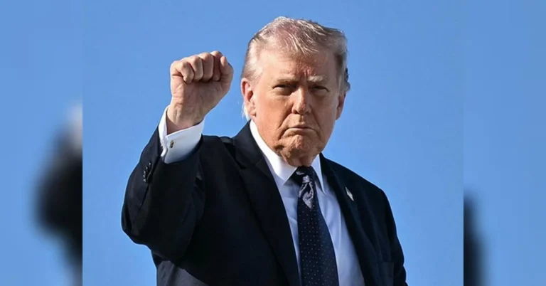 Дональд Трамп у темному костюмі підняв кулак на тлі блакитного неба