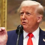 Дональд Трамп у синьому костюмі говорить у мікрофон і жестикулює рукою