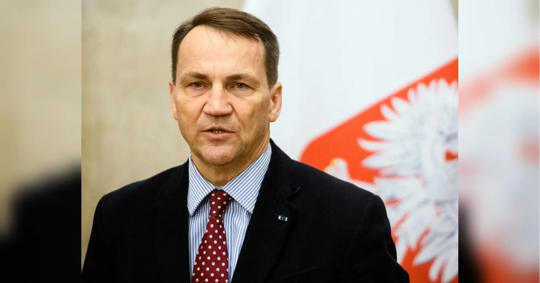 Радослав Сікорський у костюмі на тлі польського прапора з орлом