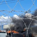 Пожежа з чорним димом за огорожею з колючого дроту на промисловому об’єкті