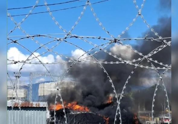 Пожежа з чорним димом за огорожею з колючого дроту на промисловому об’єкті