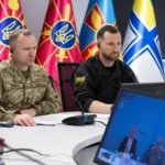 Драпатий і представник Міноборони за столом на відеонараді з прапорами