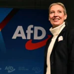 Аліса Вайдель усміхається біля синього банера партії AfD