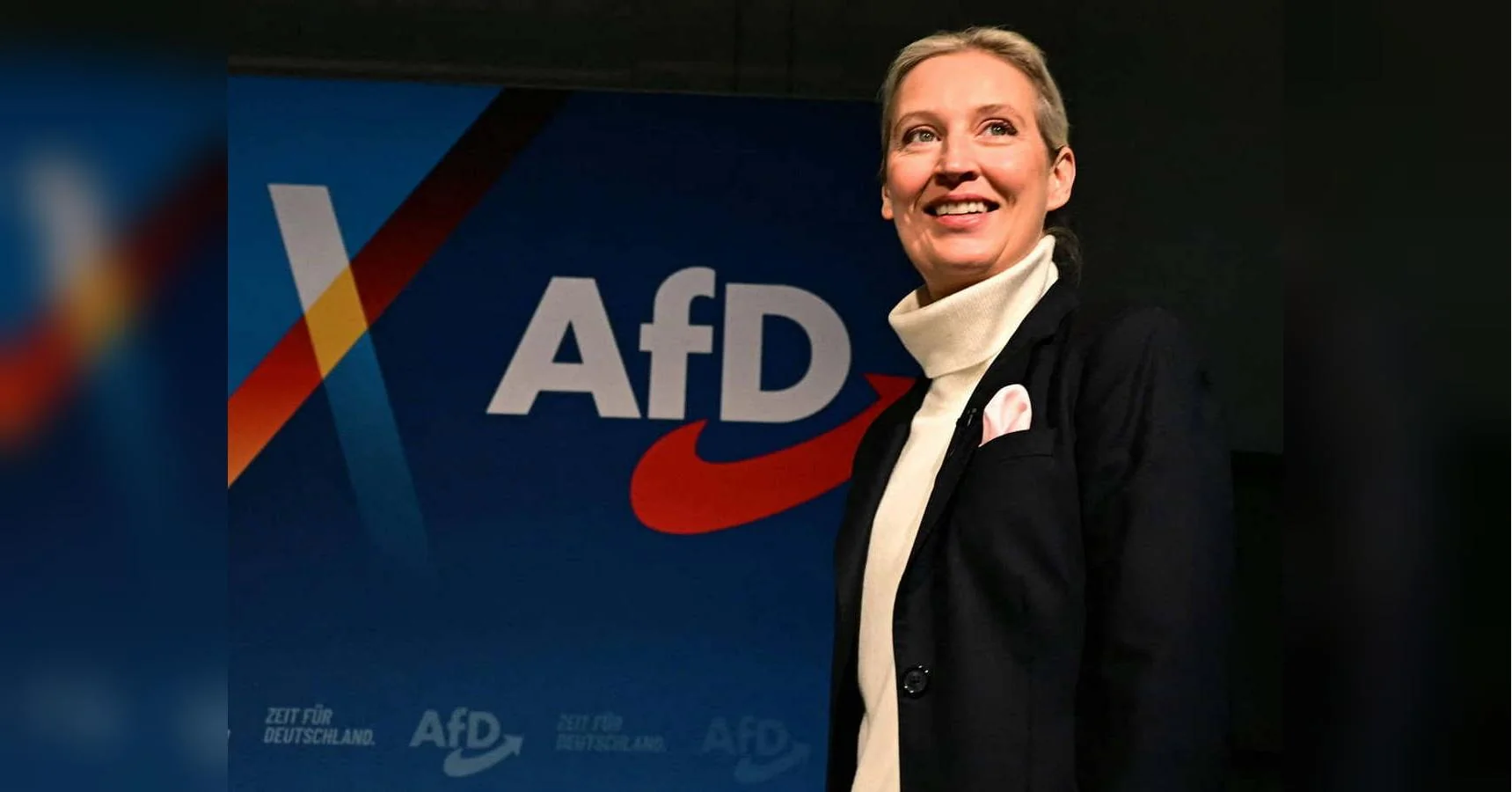 Аліса Вайдель усміхається біля синього банера партії AfD