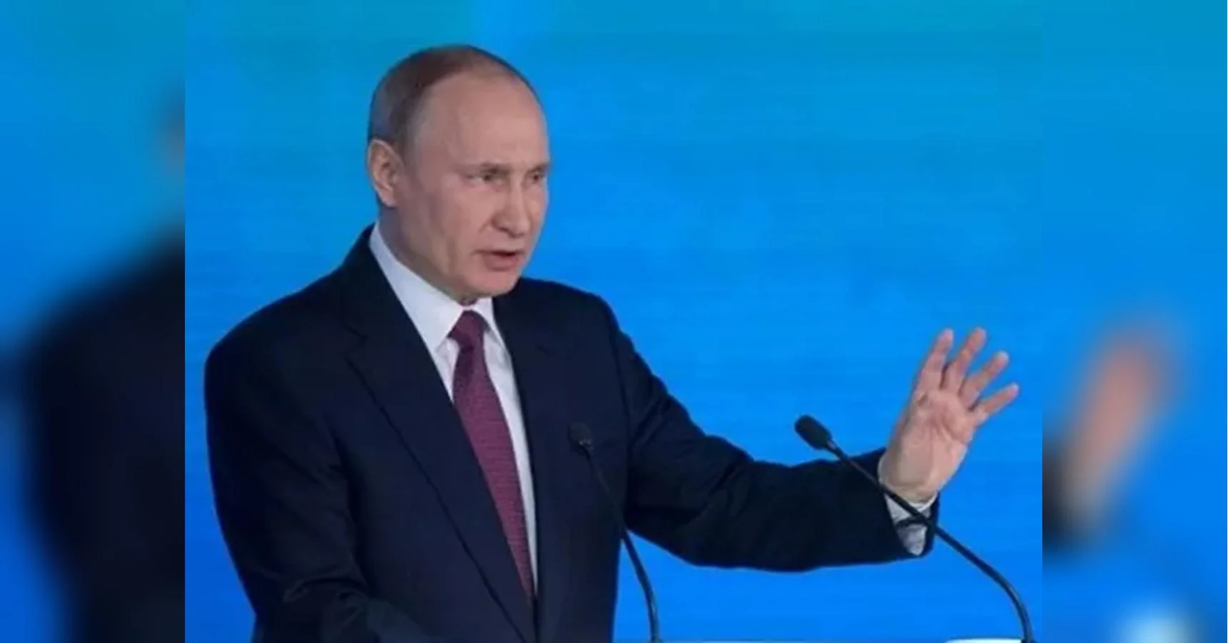 Володимир Путін виступає на трибуні з мікрофонами на синьому тлі
